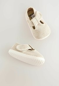 Paire de chaussures beige pour tout-petits avec tissu texturé, semelles en caoutchouc blanc et fermetures scratch sur fond clair uni.