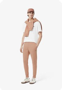 Ljusrosa joggers med en matchande rosa tröja över en vit t-shirt, avslutat med en rosa keps och vita sneakers med subtila accenter.