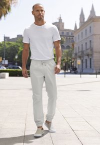 Witte T-shirt met korte mouwen gecombineerd met lichtgrijze joggingbroek met een elastieken tailleband en omslagmanchetten, aangevuld met casual instap schoenen.