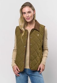 Quiltet grønn vest med en brun kordfløyelskrage, med trykknapper og et brodert detalj, båret over en beige langermet topp.