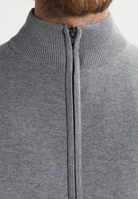 Gray knitted sweater featuring a high, ribbed collar and a front zipper, with a smooth texture and a fitted design.