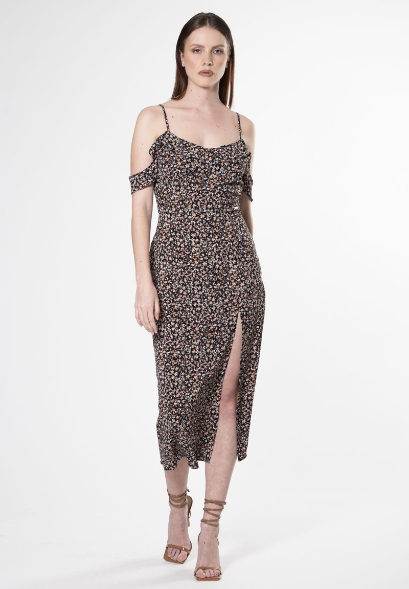Schwarzes Midikleid mit floralen Mustern, schulterfreien Ärmeln, gerafftem Oberteil, Schlitz vorne und taillierter Silhouette. Tragen mit nude-farbenen Riemchenheels.