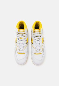 Sneakers bianchi alte con accenti gialli, caratterizzati da una tomaia in pelle liscia, colletto imbottito e suole testurizzate. Logo "New Balance" ben visibile.