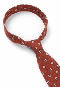 Red tie with a textured fabric featuring a pattern of white circles with black centers, knotted at the front for a polished look.