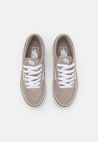 Beige semskede sneakers med hvite snører og sideaksenter, rund tå, polstret krage og Vans-logo på tungen og siden. Svart såle.