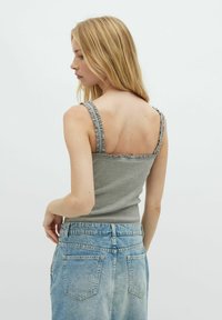 Hallide rihmadega hall tank top, keha lähedane disain. Kombinatsioonis kõrge vöökohaga heleda sinise teksaseelikuga, millel on tagakotid ja pleekinud viimistlus.