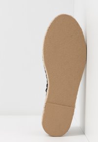 Espadrille noire avec une tige en tissu texturé, une semelle intermédiaire enveloppée de jute et une semelle extérieure en caoutchouc présentant un motif d'adhérence détaillé.