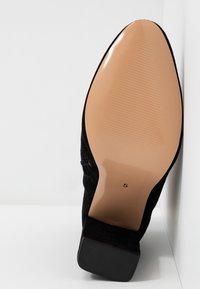 Chaussure à talon haut en daim noir avec un bout pointu et une semelle beige clair. Le talon est texturé et la semelle présente un motif rainuré. Taille indiquée : 5.
