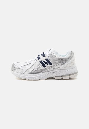 Chaussure de course athlétique blanche et argentée avec logo New Balance bleu marine et semelle amortie, vue de côté sur un fond uni.