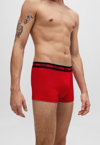 Boxers en coton rouges avec une taille élastique noire portant le logo "HUGO". Coupe ajustée et texture lisse, présentés de côté.