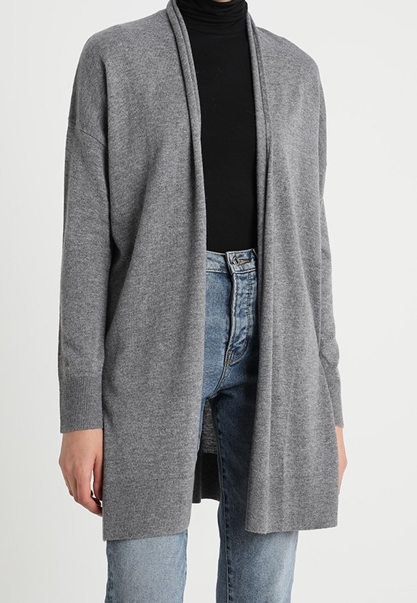 Personne portant un long cardigan gris ouvert sur un col roulé noir et un jean taille haute bleu clair.