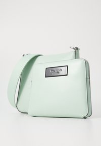 Borsa a tracolla in pelle verde menta con chiusura a zip, ferramenta nera e targhetta con logo frontale. Presenta una forma rettangolare elegante e una tracolla regolabile.