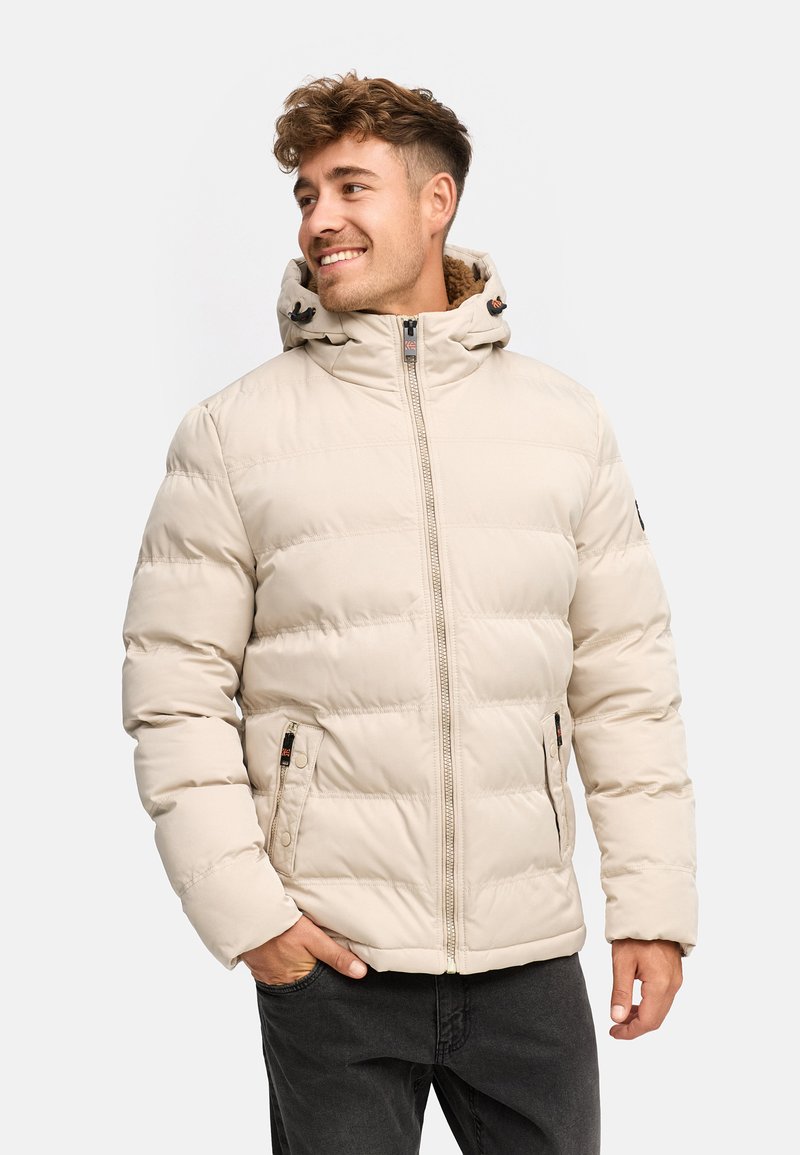 Veste rembourrée beige avec un col haut et une capuche réglable. Présente des coutures horizontales, des poches zippées et une texture lisse.