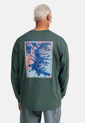 Langarm T-shirt van donker groen katoen. De achterkant heeft een grafische kaartontwerp in blauw en roze met de tekst "Free the wild".