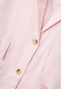 Gaišpinky lins bārkstis ar divām priekšējām kabatām un vienu pogu aizdari, izgatavots no gludas, nedaudz strukturētas auduma.