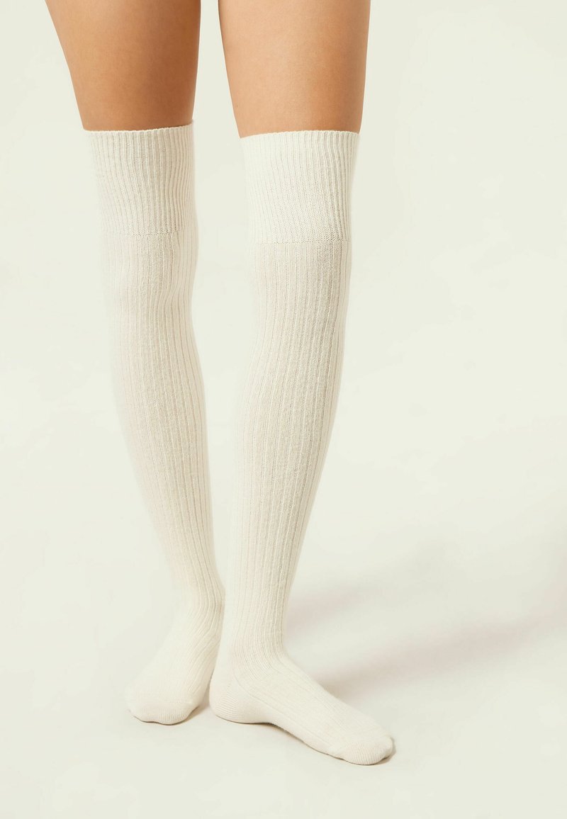Knielange geribde sokken in off-white, gemaakt van zacht materiaal, met een gestructureerd ontwerp dat aan de bovenkant goed aansluit en een glad voetgedeelte heeft.