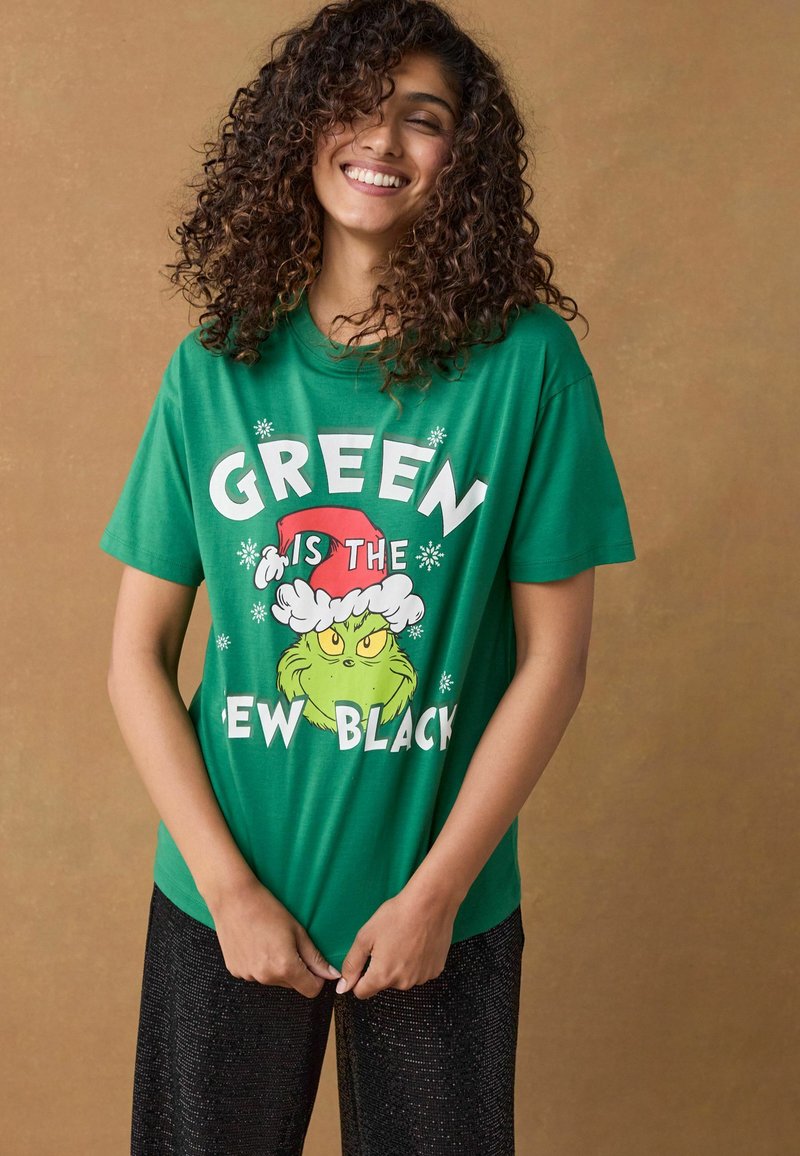 Groene katoenen t-shirt met de tekst "GREEN IS THE NEW BLACK" en een afbeelding van de Grinch in een kerstmanmuts. Korte mouwen, relaxte pasvorm.