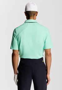 Kortärmad polo skjorta i mintgrön med en traditionell krage, tillsammans med marinblå byxor och en vit keps; har en slät tygkvalitet.