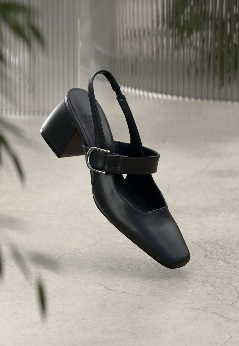 Černé kožené sandály na podpatku s čtveratou špičkou, se sponou a blokovým podpatkem, vystavené na texturovaném povrchu.