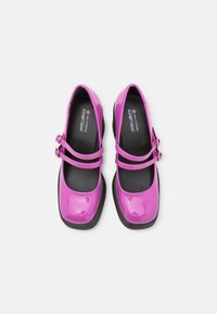 Chaussures Mary Jane en cuir patent rose avec deux sangles réglables, orteils ronds et semelle en caoutchouc noir. Présentent une texture lisse et des matériaux végan.