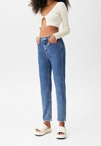 Light beige ribbed crop top, high-waisted blue denim jeans, and cream platform sandals. Fitted design with a straight leg and pockets.
