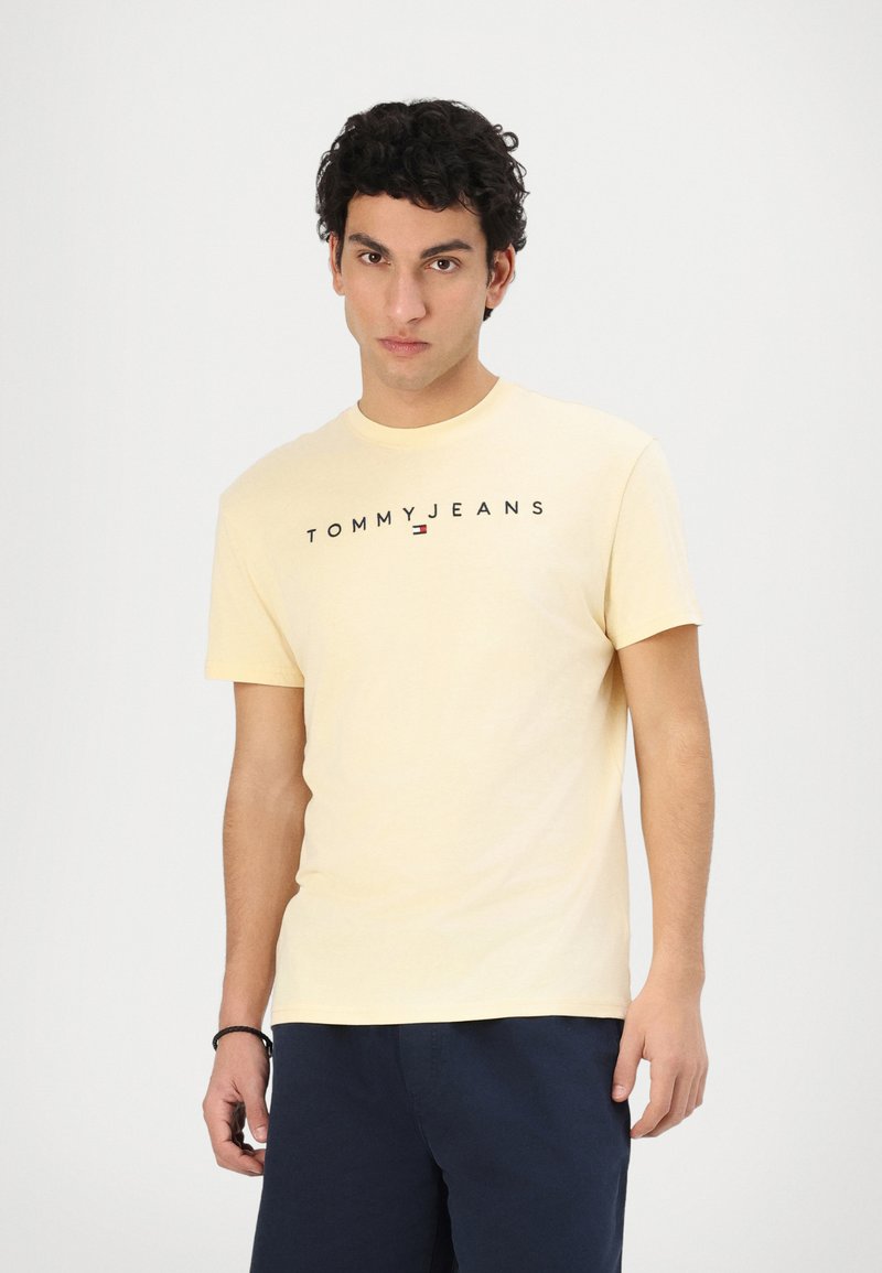Gelbes Baumwoll-T-Shirt mit Rundhalsausschnitt und kurzen Ärmeln, mit "TOMMY JEANS" in Schwarz über der Brust bedruckt.