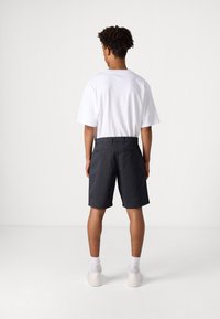 Men's white cotton T-shirt paired with dark gray knee-length shorts featuring side pockets and back button details. White sneakers.