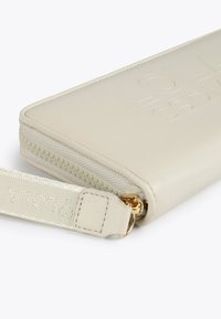 Cartera de cuero beige claro con logotipo en relieve, herrajes dorados, cierre de cremallera y correa de tela. Textura suave y forma rectangular.
