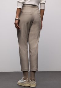 Beige, verjüngte Hose mit glatter Textur, zwei Gesäßtaschen und einem elastischen Bund, kombiniert mit hellen Sneakers und gerippten Socken.