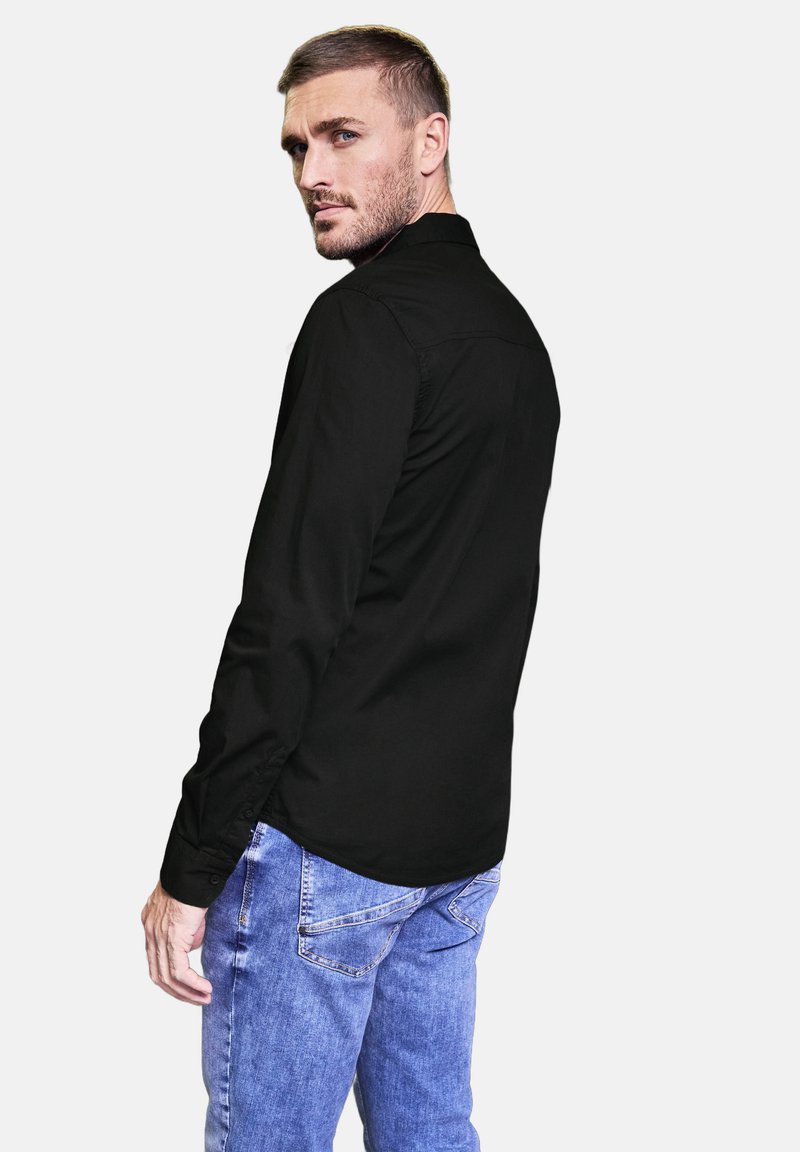 Zwarte langwerpige blouse met een geknopt kraagje, een soepele textuur en knoopmanchetten, gecombineerd met lichtblauwe denim jeans.