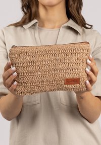 Woven beige Tasche aus natürlichen Fasern, mit strukturierter Oberfläche, Reißverschluss und einem kleinen Leder-Logo-Patch.