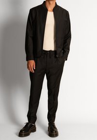 Czarna kurtka bombowiec z wysokim kołnierzem, zestawiona z czarnymi zwężającymi się spodniami. Teksturowana tkanina, zamek błyskawiczny z przodu kurtki, spodnie z regulowanym pasem.