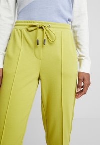 Light green sweatpants featuring a drawstring waist with black accents, side pockets, and pleats for added texture.