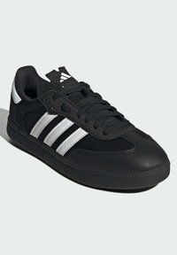 Czarne sportowe buty z teksturowaną cholewką, z trzema odblaskowymi srebrnymi paskami po bokach, oraz gumową podeszwą z wzorzystym bieżnikiem.