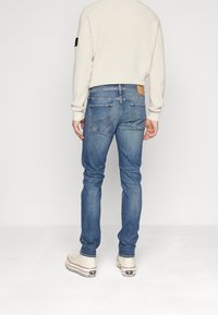 Blå denimjeans med slim fit, medelhög midja och bakficka. Har typiska bakfickor och en subtil blekt textur.