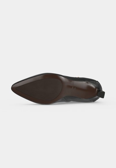 Zapato puntiagudo de cuero negro elegante visto desde la suela, mostrando una suela marrón oscuro lisa y una pequeña lengüeta en el talón en la parte trasera.