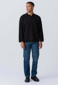 Sort, langærmet polo shirt med rabatkrave, parret med blå lige ben jeans og sorte sko. Enkel design, uden synlige mønstre.