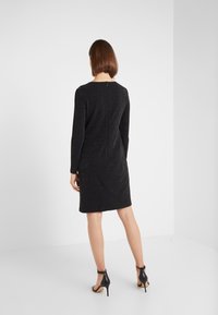 Black, long-sleeve dress with a fitted silhouette, textured fabric featuring subtle sparkles, and a rear zipper closure.