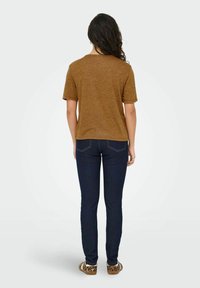 Bruine korte mouwen t-shirt met een ronde hals, gecombineerd met donkerblauwe slim-fit jeans en slip-on schoenen met dierenprint, gezien van achteren.