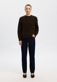 Barna kötött kardigán kerek nyakkal, gombos záródással és hosszú ujjal, sötétkék egyenes szárú farmerrel és barna magassarkúval párosítva.