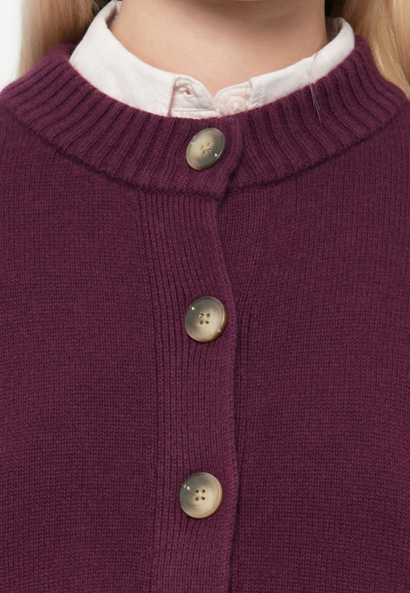 Fioletowy sweter dzianinowy z prążkowanym kołnierzem, z trzema okrągłymi, teksturowanymi guzikami i gładką powierzchnią materiału.