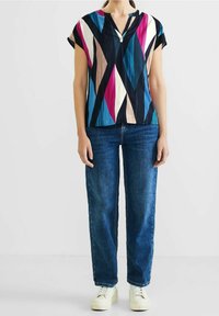 Blouse à manches courtes en bleu marine avec un motif géométrique vibrant de rose, de bleu-vert et de crème. Elle présente un décolleté en forme de keyhole et est fabriquée en tissu léger.