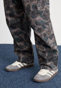 Pantalones con estampado de camuflaje en tonos grises y azules, combinados con zapatillas de ante grises que tienen rayas blancas y una suela de goma texturizada.