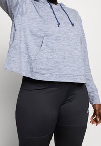 Helles blaues, meliertes Hoodie mit einem cropped Design, Kordelzugkapuze und Fronttasche, kombiniert mit schwarzen Leggings mit strukturierten Einsätzen.