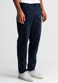 Navyblauwe katoenen broek met een relaxte pasvorm, voorzien van zijzakken en een soepele textuur, gecombineerd met witte sneakers.