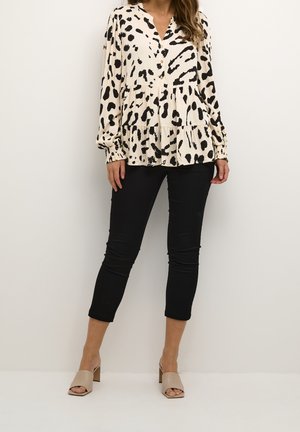 Kermanvärinen pusero, jossa musta eläinkuosi, kerroksellinen malli ja pitkät hihat. Yhdistetty mustiin kapeisiin farkkuihin ja beigen sävyisiin avokärkisiin korollisiin sandaaleihin.