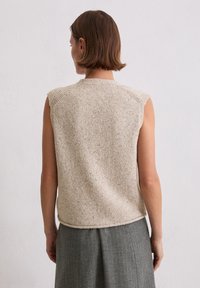 Beiges gestricktes ärmelloses Oberteil mit strukturiertem Muster und abgerundetem Saum. Die Schulternähte sind mit kleinen Details versehen und ergänzen einen grauen Rock.