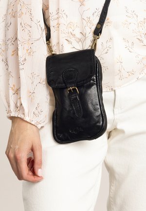 Black leather crossbody bag with a flap closure, brass hardware, and a zippered pocket. Smooth texture and rectangular shape.