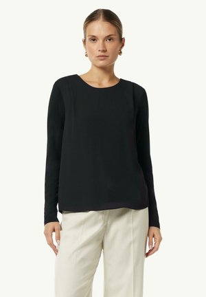 Black long-sleeve top with a round neckline, made of smooth fabric, featuring a slightly loose fit and a curved hemline, paired with beige trousers.