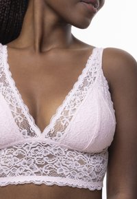 Bralette en dentelle rose pâle. Caractéristiques : décolleté en V, motifs floraux en dentelle, doublure douce et bords festonnés le long des bretelles et de l'ourlet.
